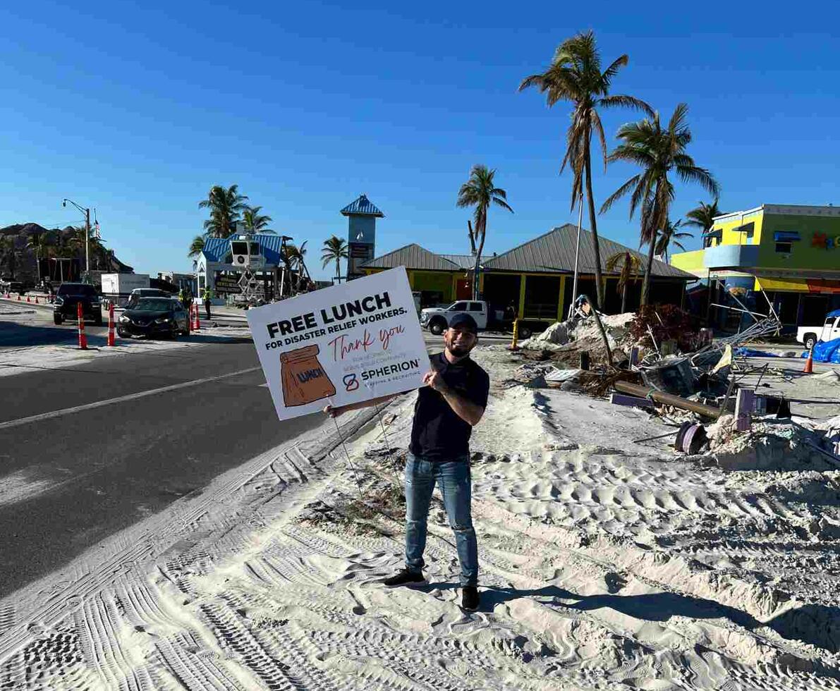 Man standing on a beach near a street holding a sign that reads, "Free Lunch."
