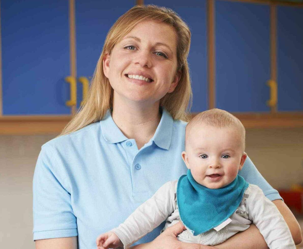 Daycare assistant smiling while holding a baby
