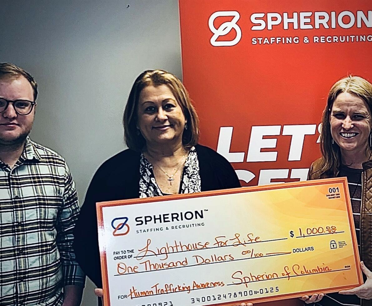 Close up of three people holding a large check with an orange Spherion banner background