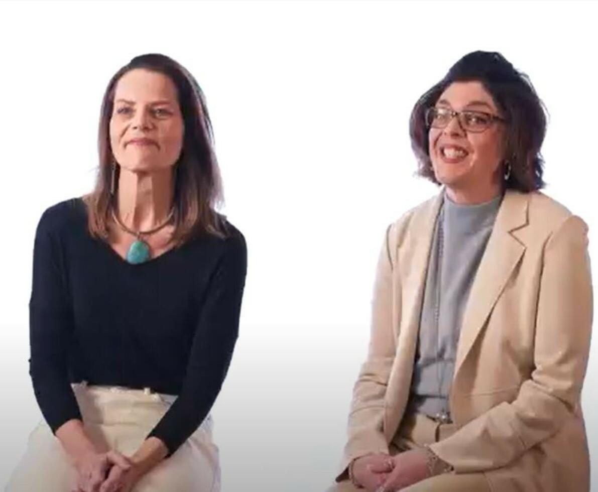 Two women sitting together on a white background