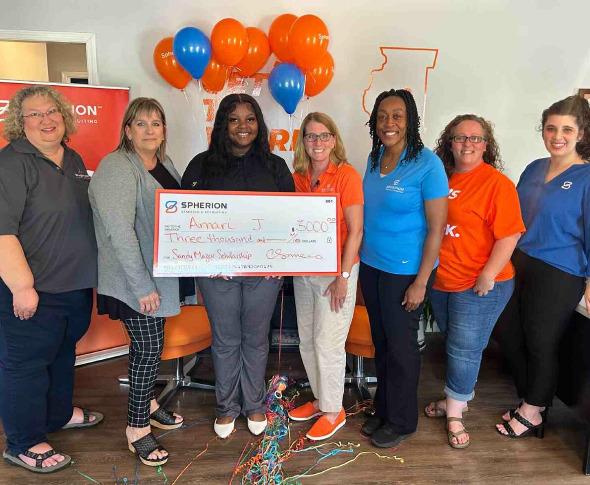 A group of women presents the woman in the middle with a giant check for a scholarship