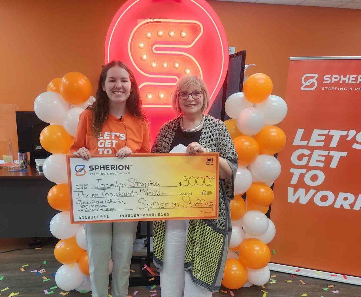 Two women standing in front of orange balloons and an orange S sign holding a giant orange check