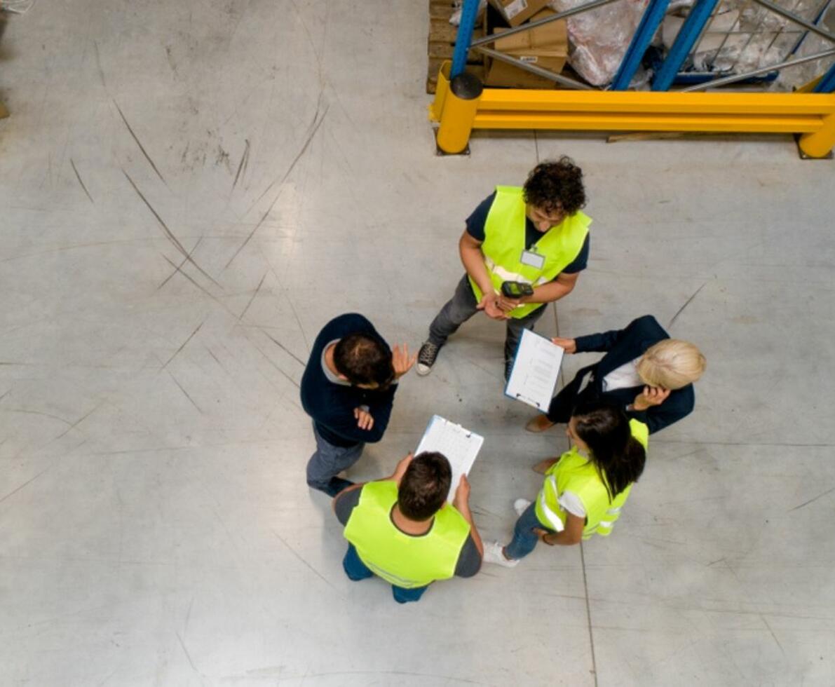 A birds-eye view of a group of warehouse workers in yellow vests gathering in a warehouse
