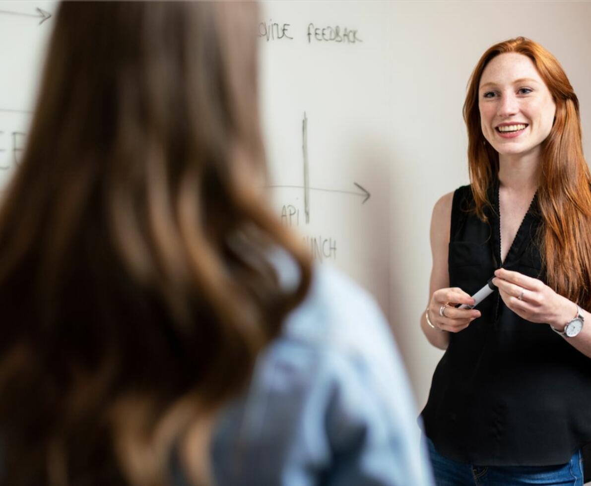 A red-haired woman smiling and talking to another woman in the foreground