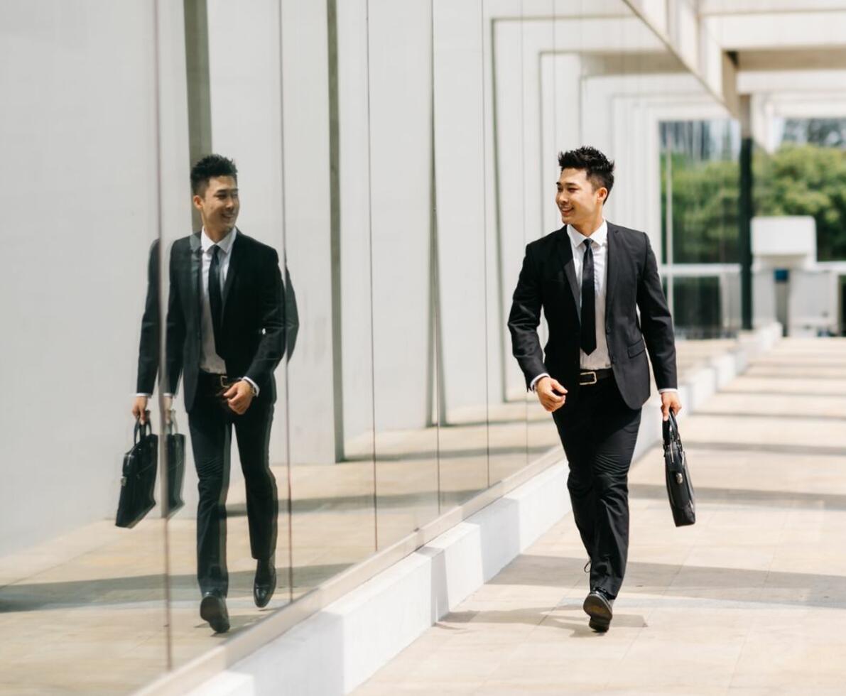 A suited man walking with a briefcase while looking at his reflection