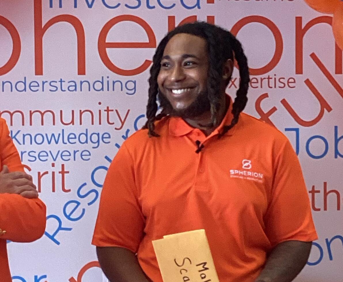A smiling African-American man in an orange shirt holding a manila envelope