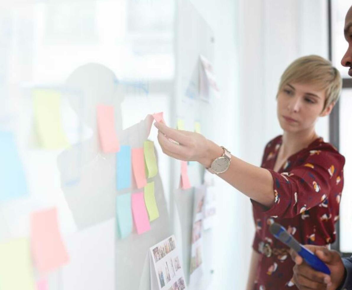 A woman and man arranging sticky notes on a whiteboard