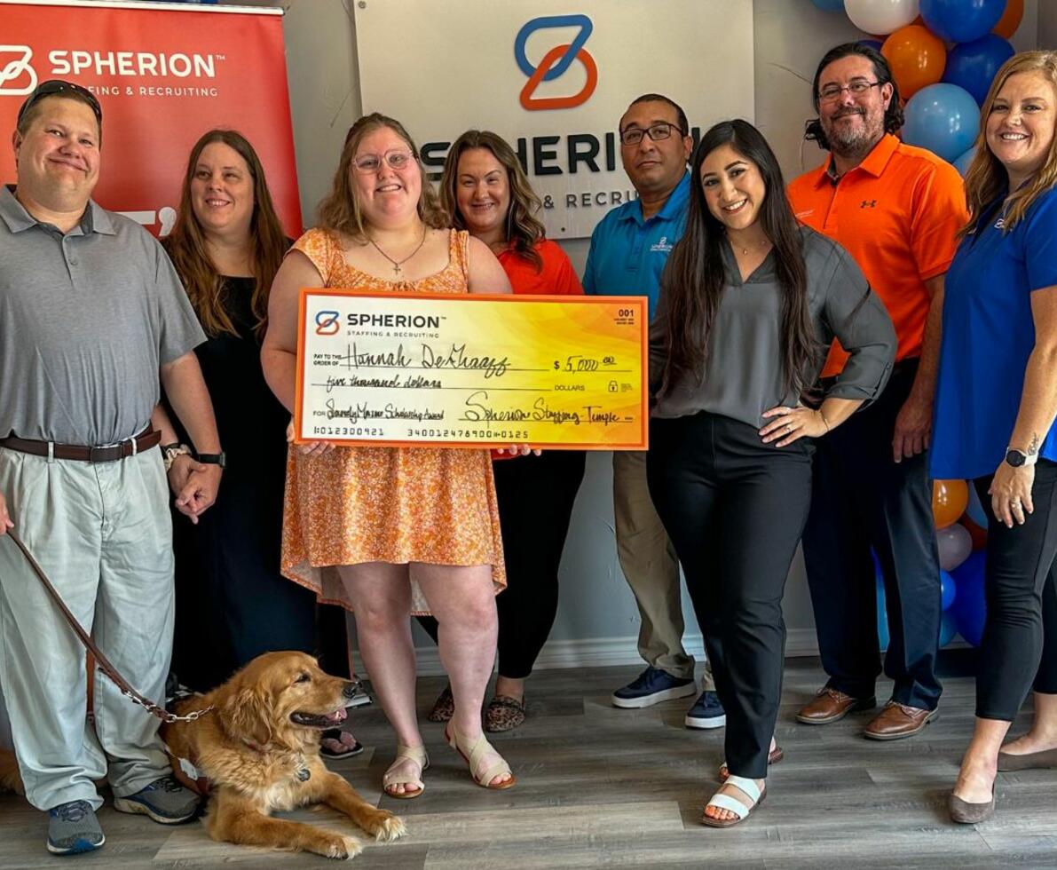 A group of people celebrating a girl holding a giant orange check