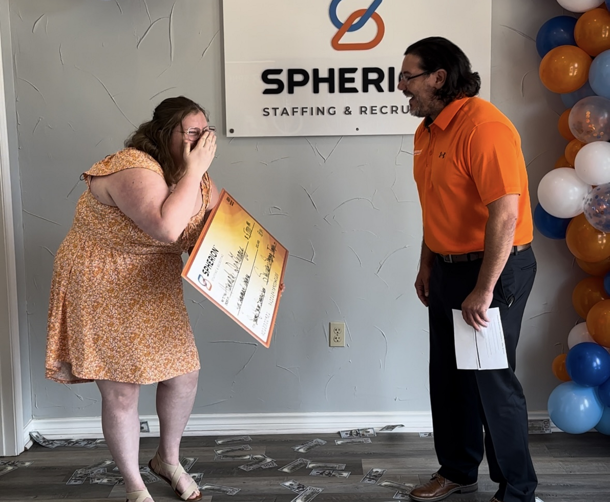 A girl in an orange dress and a man in an orange shirt standing in front of a colorful balloon arch