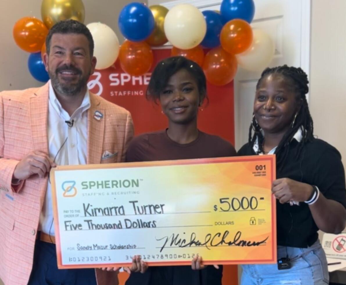 Three people smiling and holding a giant orange check