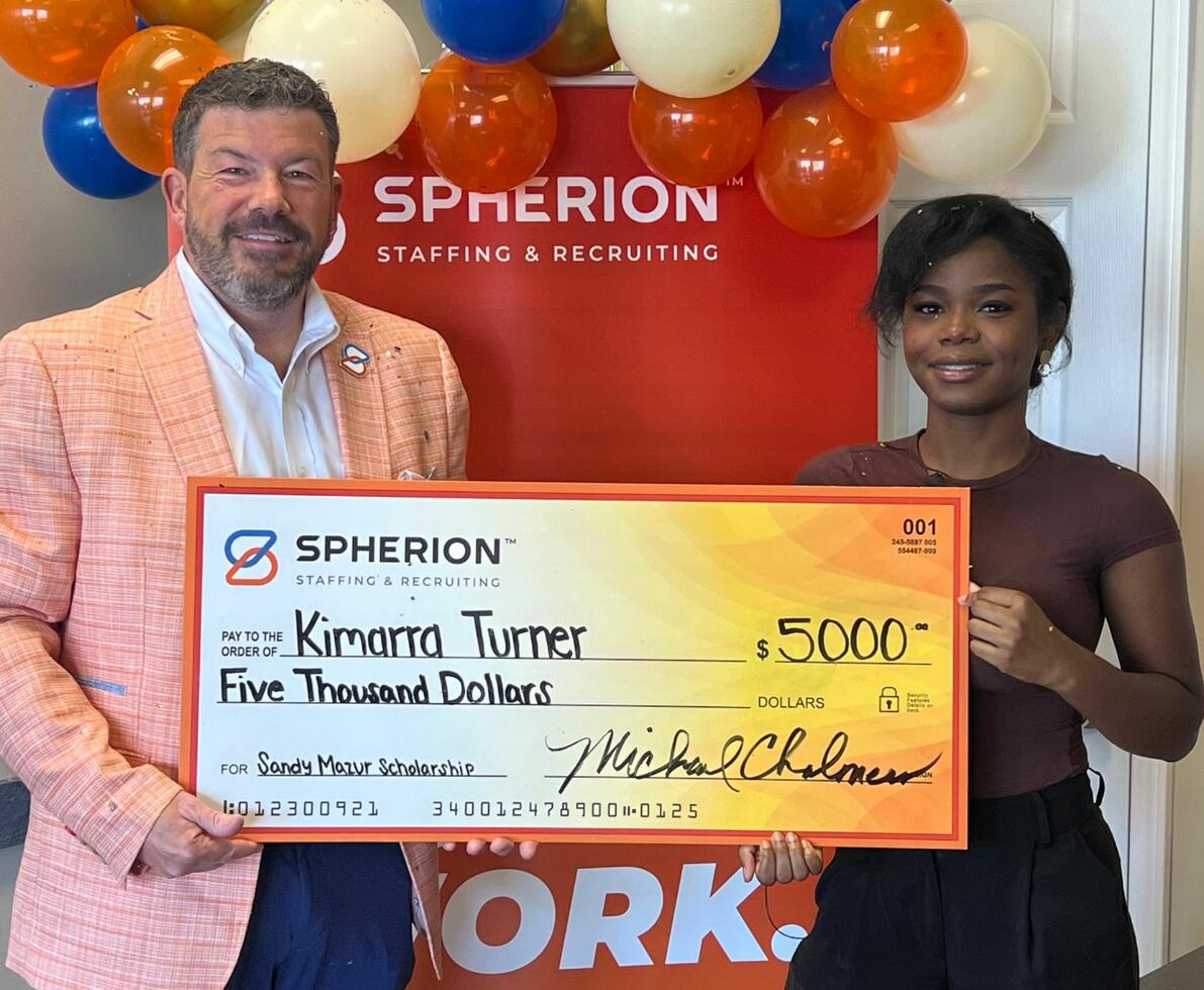 A man and a girl smiling while holding a giant orange check