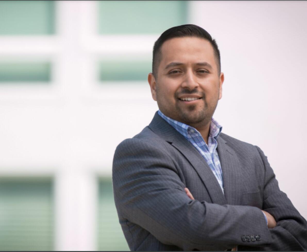 A Hispanic man in a suit with his arms crossed
