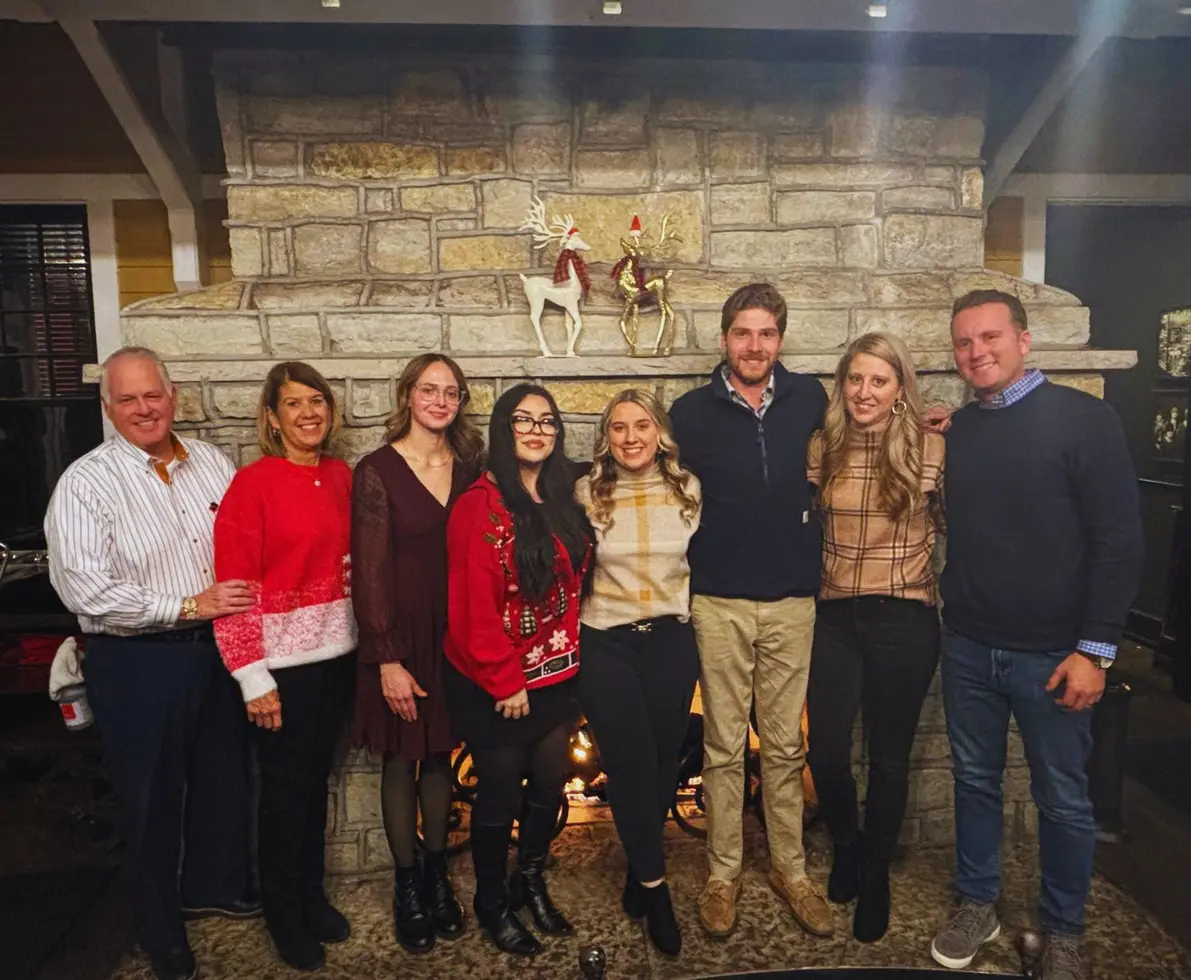 A group of people smiling and standing in front of a decorated fireplace