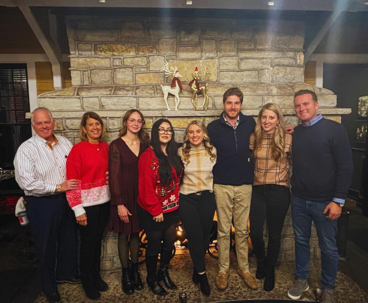 A group of people smiling and standing in front of a decorated fireplace