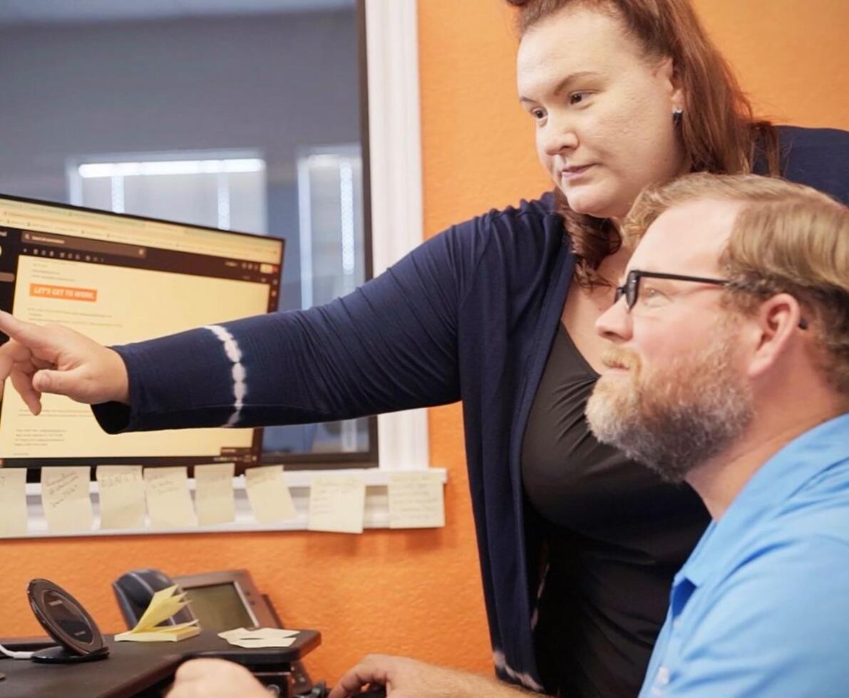 A woman showing a man how to apply on a computer