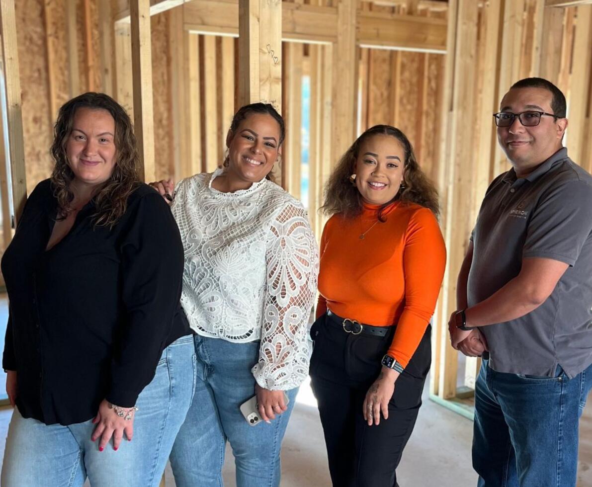 Four Spherion professionals standing and smiling in a framed-out building