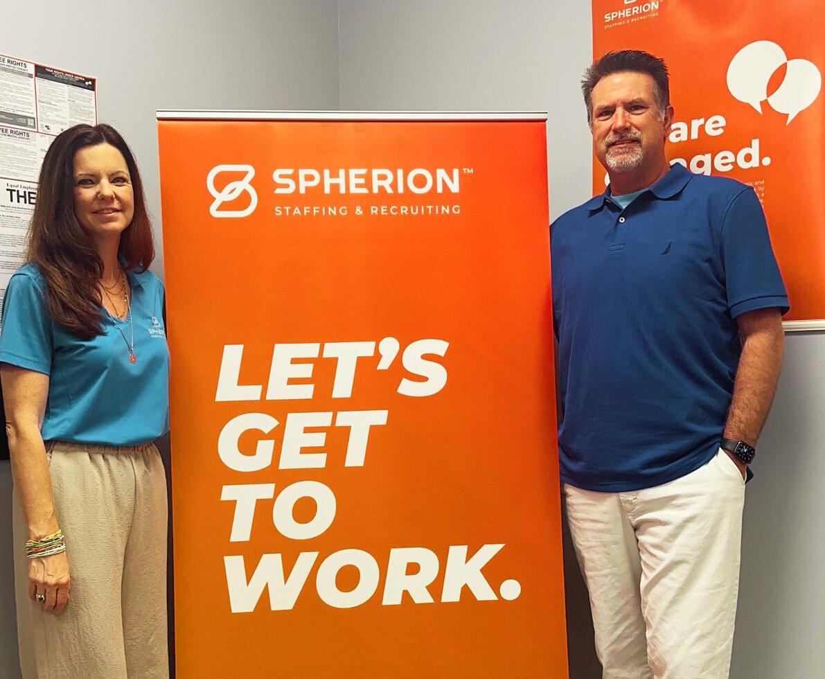 Two Spherion professionals standing by an orange sign that reads, Let's Get to Work