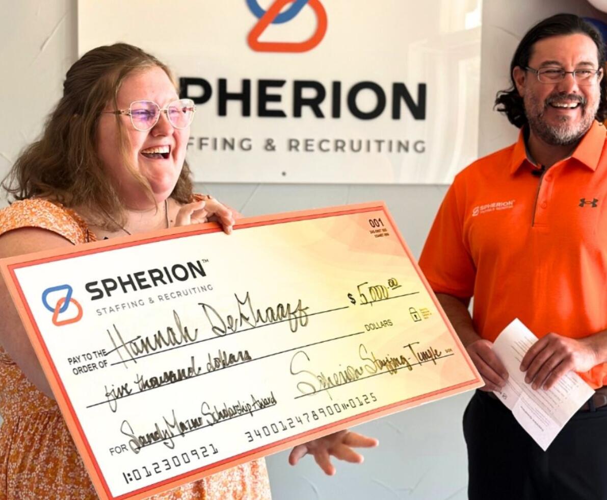 Photo of a young woman smiling and holding a big check next to a man in an orange shirt