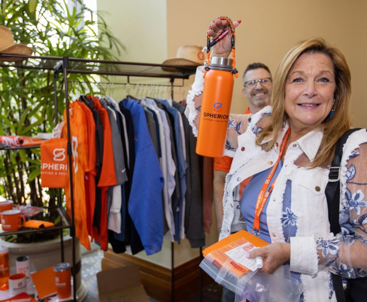 A woman posing n front of a rack of orange and blue clothing