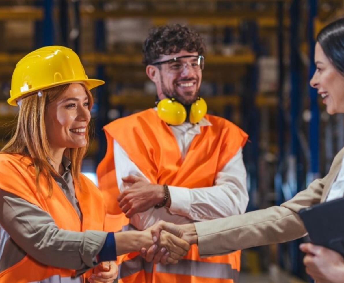 Warehouse workers in safety vests and hard hats greet a manager