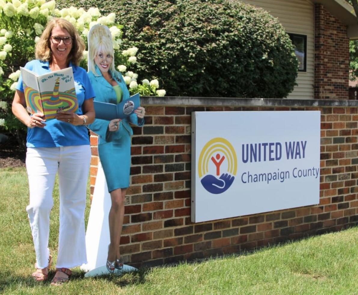A woman holding a book next to a cutout of Dolly Parton and a sign for the United Way of Champaign County