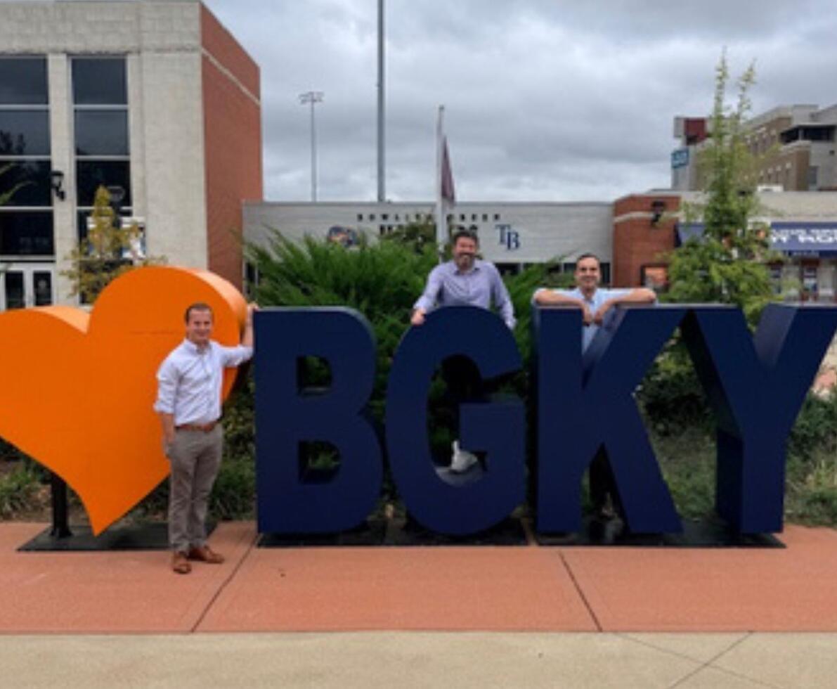 A group of professionals relaxing in front of an outdoor art installation that consists of an orange heart and the letters BGKY
