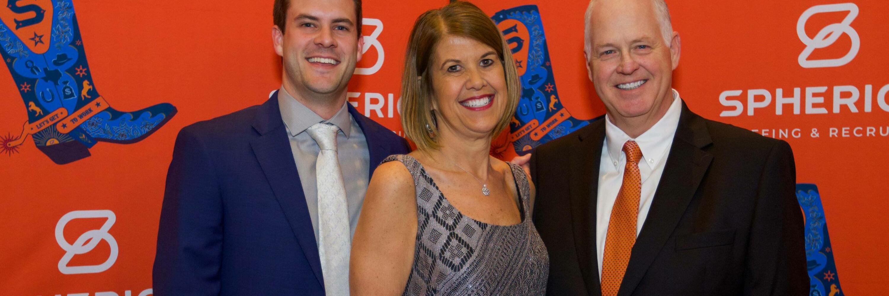 Three people smiling in front of an orange backdrop