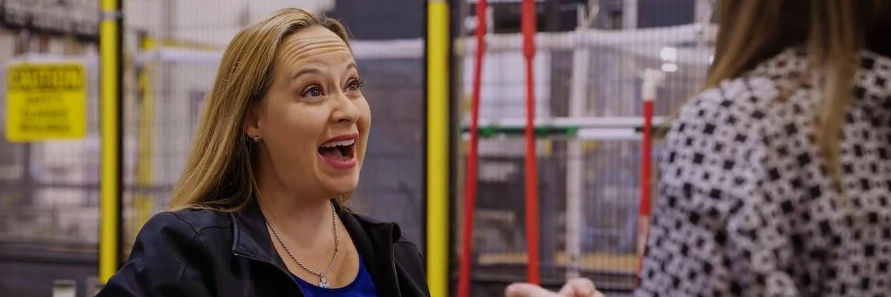 A woman in a black and blue suit smiling in a factory setting