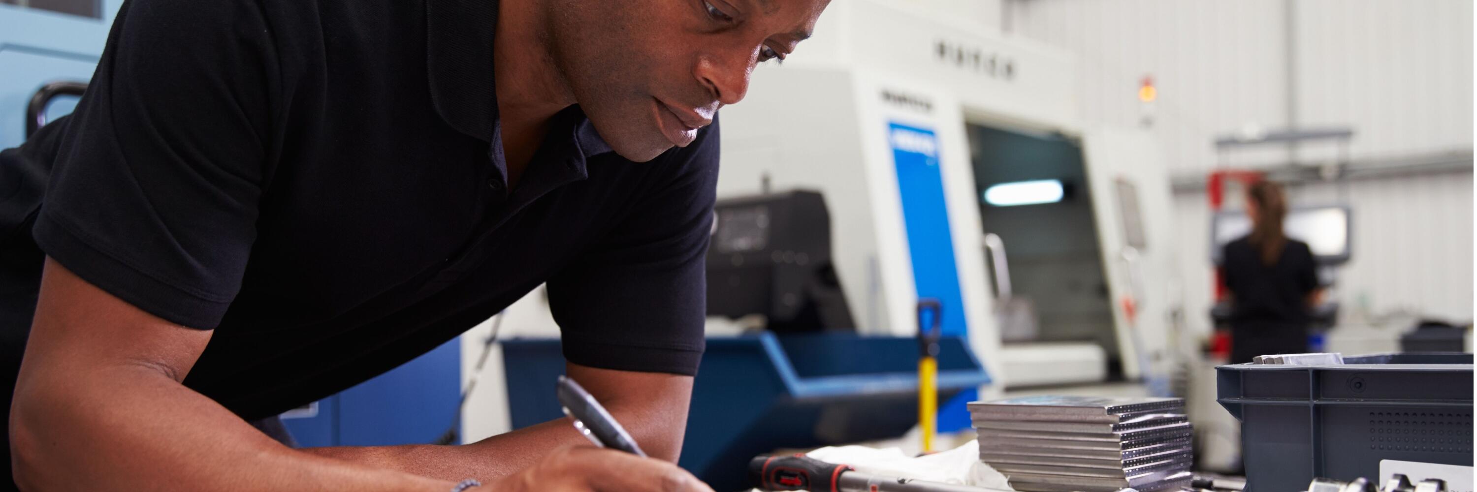 African-American male inspecting blueprints for a CNC machine