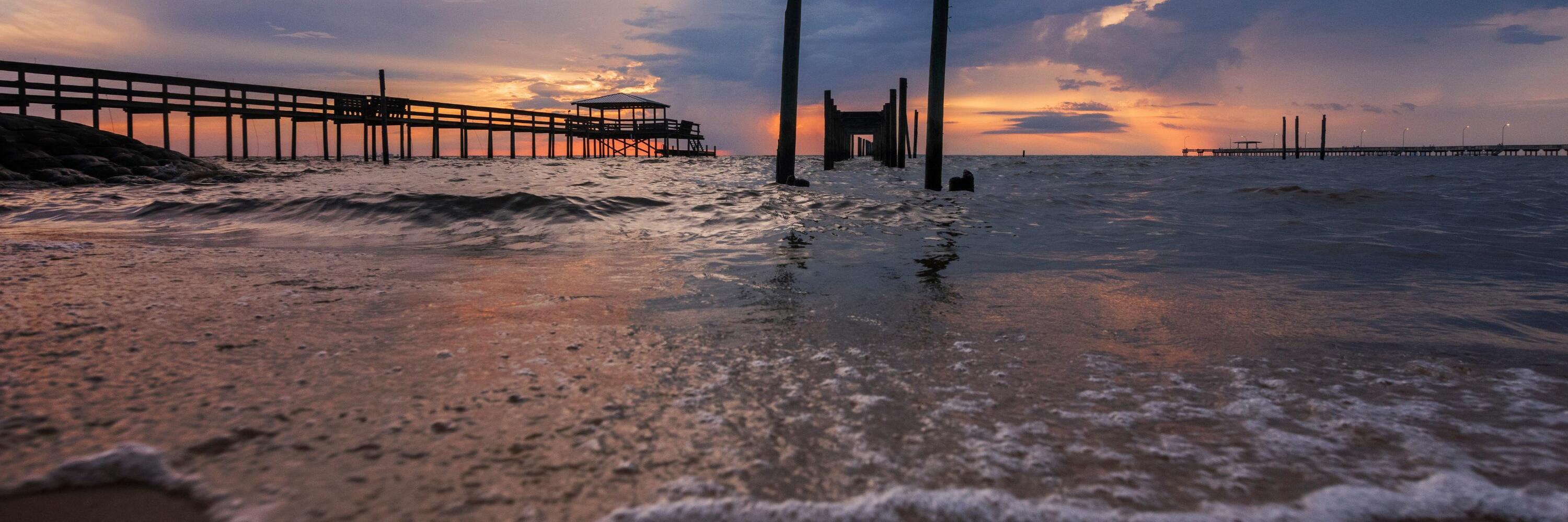 A beach with old piers extending into the water at sunset