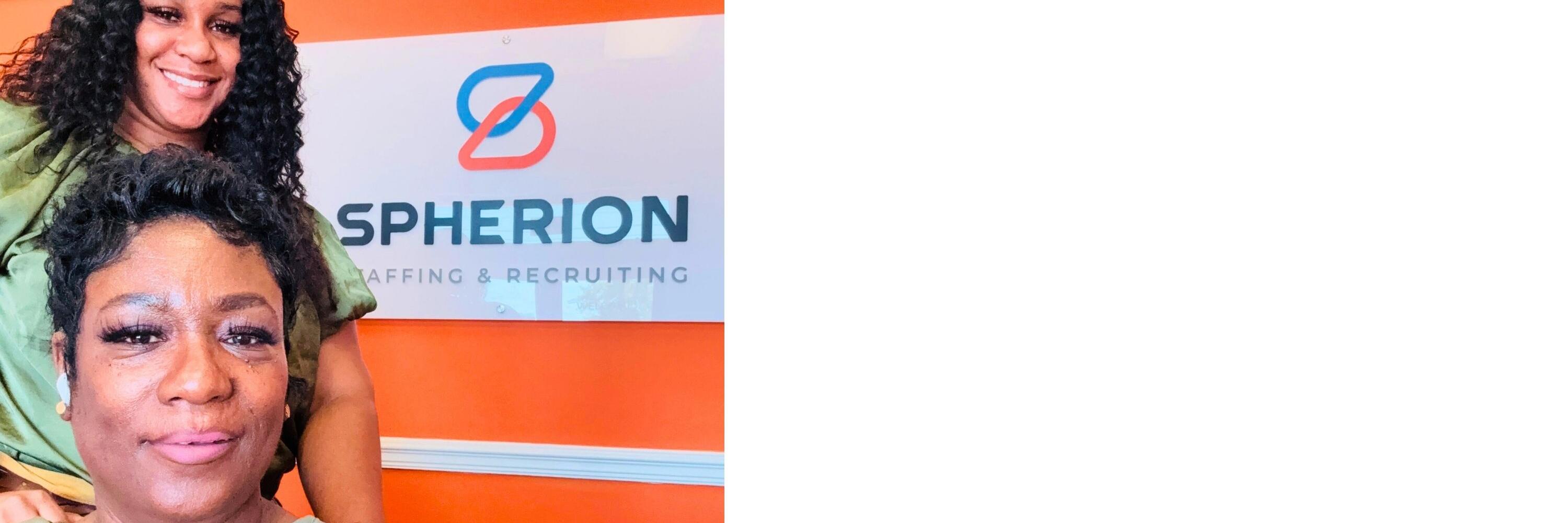 Two professional women posing in front of a Spherion sign