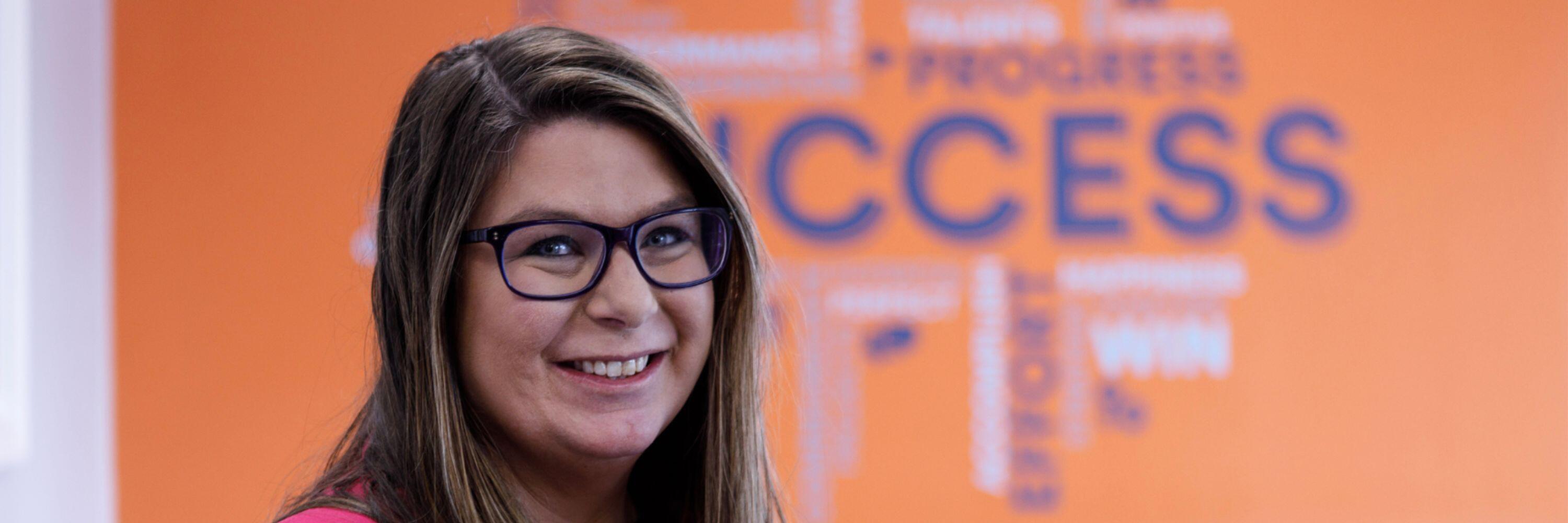 Smiling woman against an orange background with blurred words on the wall