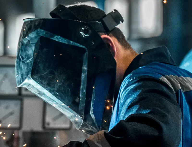 Welder wearing a blue protective face mask with sparks and machinery