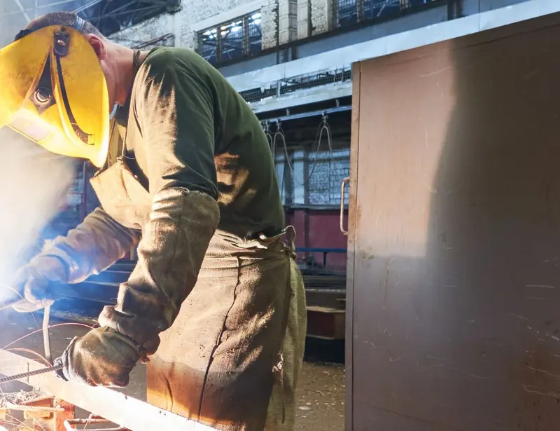 Welder in yellow protective mask using a heat tool to create a metal grid