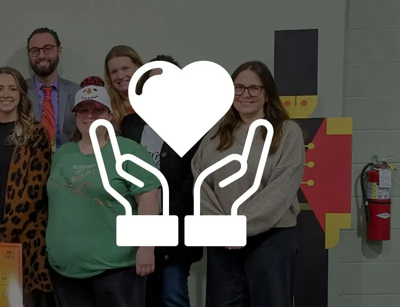 A photo of a grop of people presenting a giant check with a white heart and hands logo