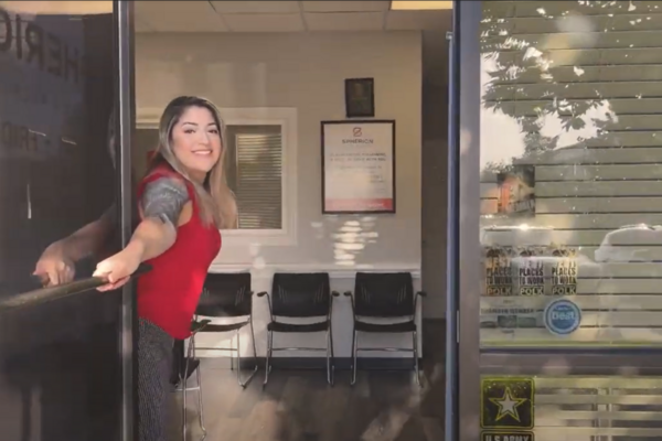 A woman in a red shirt is opening a glass door to a Spherion office. Black chairs are in the background.