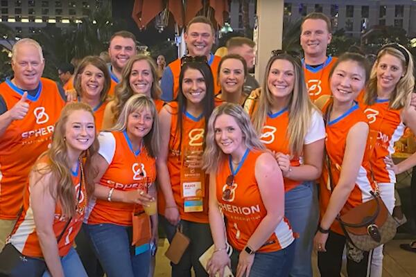 A group of Spherion colleagues smiles in orange Spherion jerseys