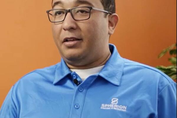 Picture of a man in a blue polo shirt against an orange background