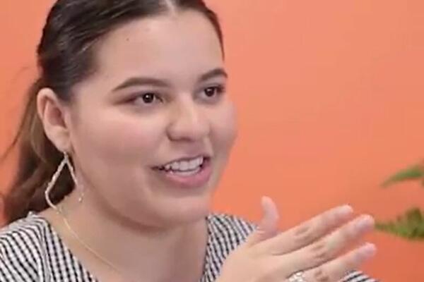 Woman smiling and gesturing in front of an orange background