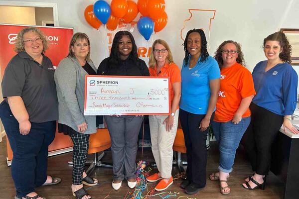 A group of women presents the woman in the middle with a giant check for a scholarship