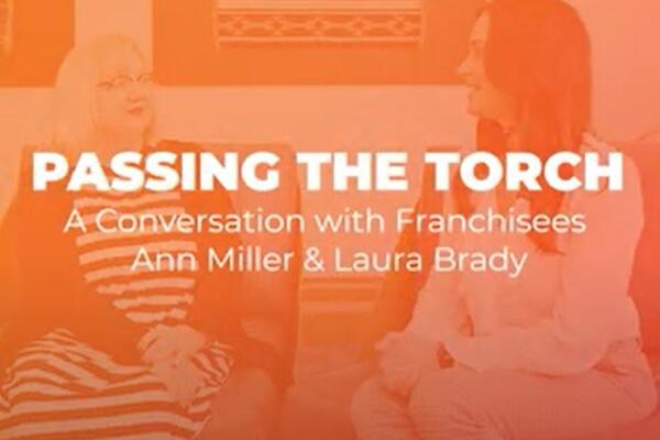 Shaded background of two women talking with the headline Passing the Torch: A Conversation with Franchisees Ann Miller & Laura Brady