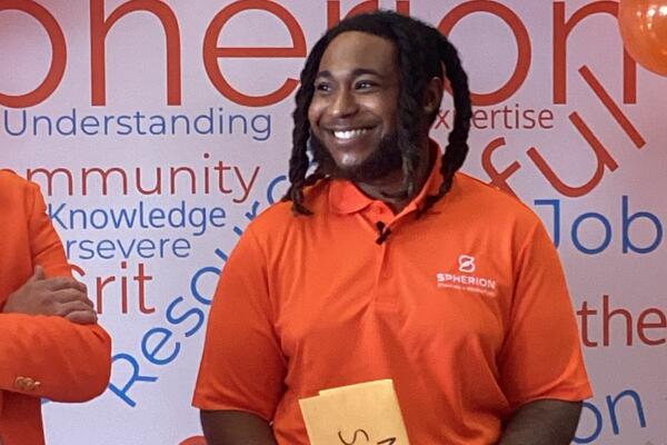 A smiling African-American man in an orange shirt holding a manila envelope