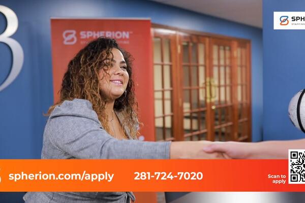 A woman in an orange and blue office setting reaching out to shake hands with a woman off camera