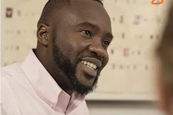 An African-American man in business casual smiles off camera against a neutral background