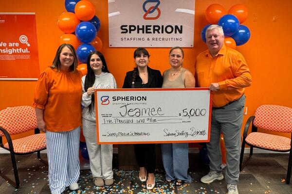 A group of people holding a giant scholarship check against an orange and blue background of posters and balloons