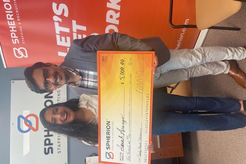 A girl and a man pose with a giant scholarship check