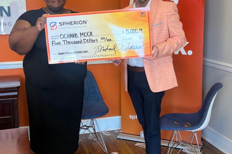A woman and a man stand smiling with a giant scholarship check