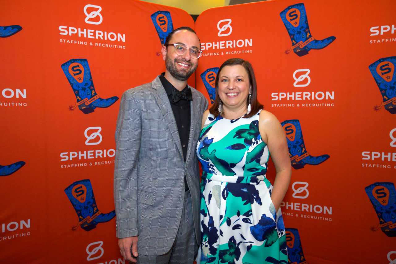 A young couple dressed up and posing in front an a Spherion-branded backdrop
