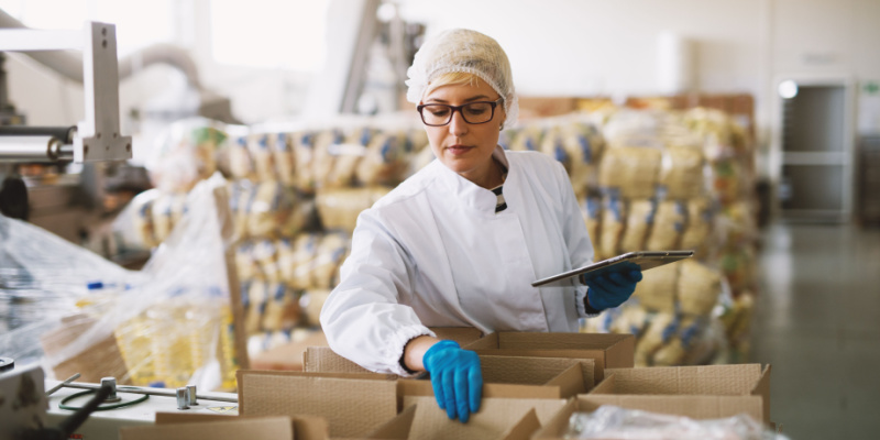 Young female employee in sterile clothes is checking packages ready to be delivered