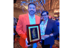 Michael Chalmers, in orange sport coat, holding a plaque, next to Kathy George, in navy blazer, both smiling at the camera